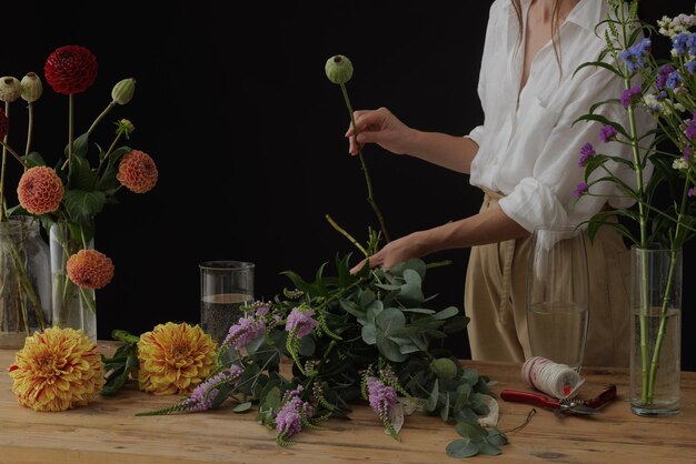 Girl florist collects a bouquet in a flower workshop on a dark background layout for floristry