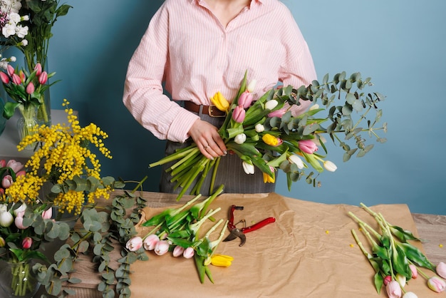 girl florist collects a bouquet of spring tulip flowers on a clean blue background