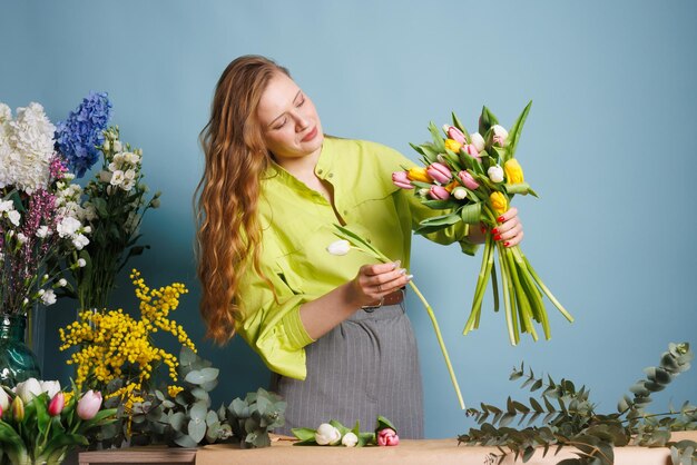 girl florist collects a bouquet of spring tulip flowers on a clean blue background