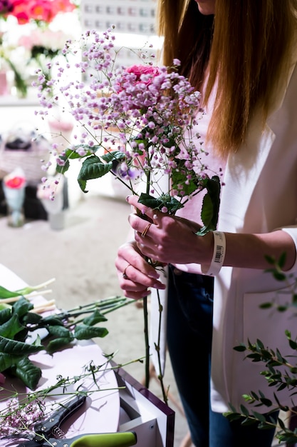 La ragazza fiorista crea un delicato bouquet di gipsofila e rose dietro al bancone nel mercato dei fiori