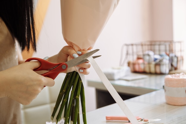 Girl florist using scissors decorates a bouquet of flowers in a flower shop