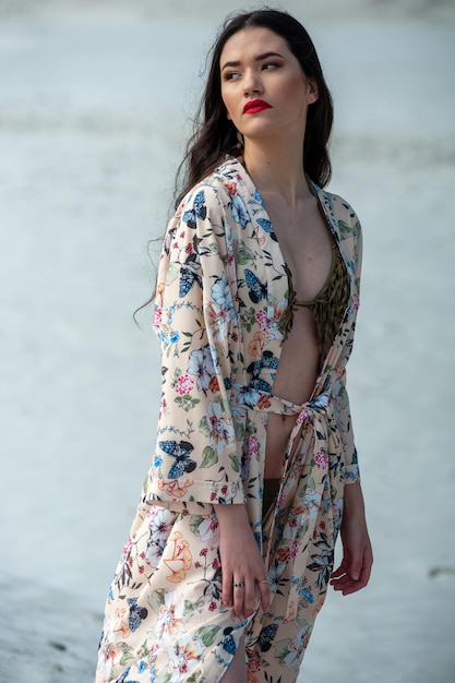 A girl in a flowered dress stands by the water.