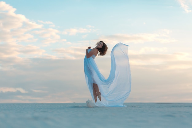 Girl in a fly white dress dances and poses in the sand