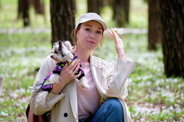 A girl in the forest with a dog and a snowdrop in her hand.