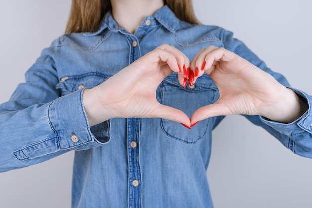 Girl forming heart with fingers on isolated gray background