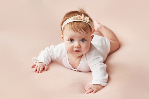 A girl of four months lies on a light pink background