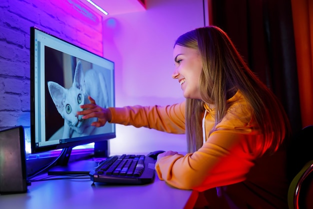 Ragazza freelance guarda sullo schermo di un computer un gatto seduto in un appartamento alla scrivania di un computer