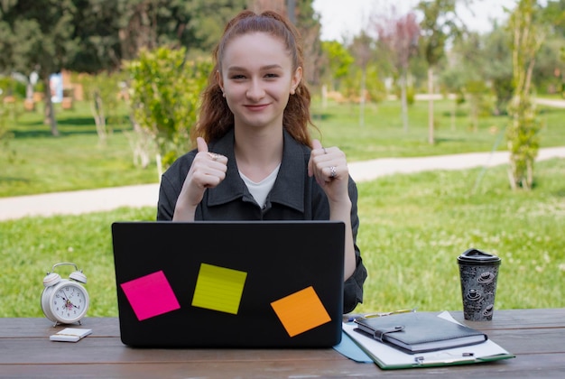 Girl freelancer student working at laptop in park showing super