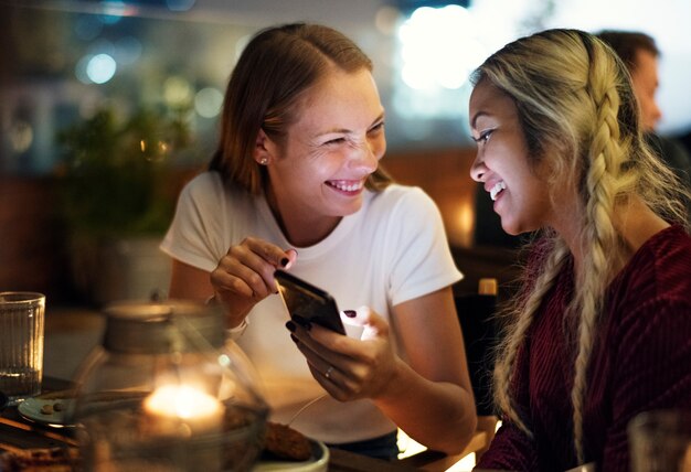 Girl friends having a dinner together at a rooftop bar using a smartphone