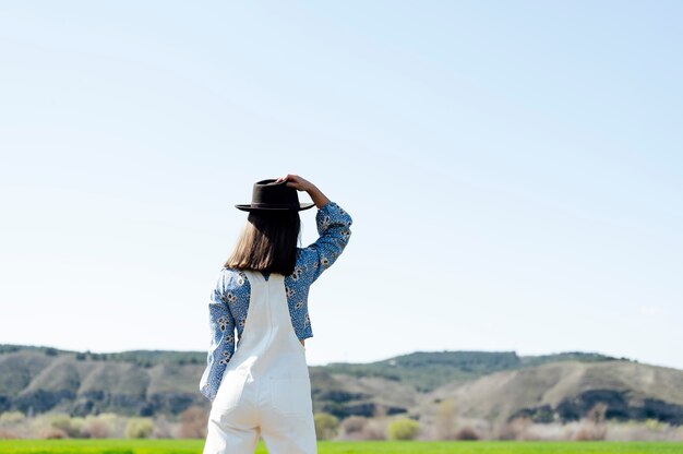 Girl from behind in a field holding a hat on a sunny day