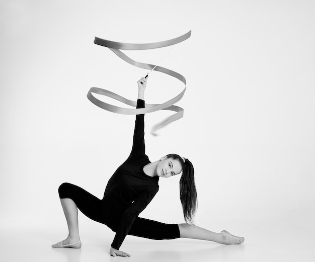 a girl from rhythmic gymnastics in a bodysuit rotates a ribbon sitting on a halfstep