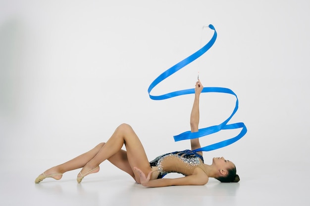 Photo a girl from rhythmic gymnastics in a bodysuit shows an exercise with a ribbon lying on her back