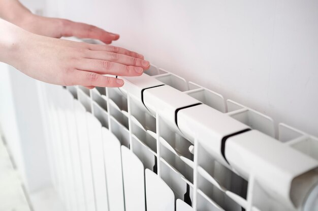 Girl froze and warms hands near white multicell radiator