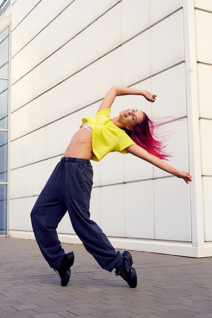 Photo girl in full-length sportswear rose on her toes, dances and trains against background of building