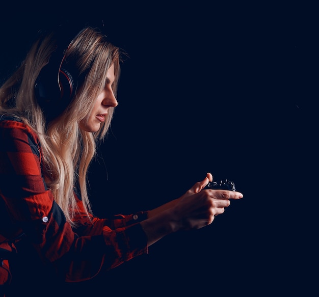 Girl gamer in headphones and with a joystick enthusiastically playing on the console