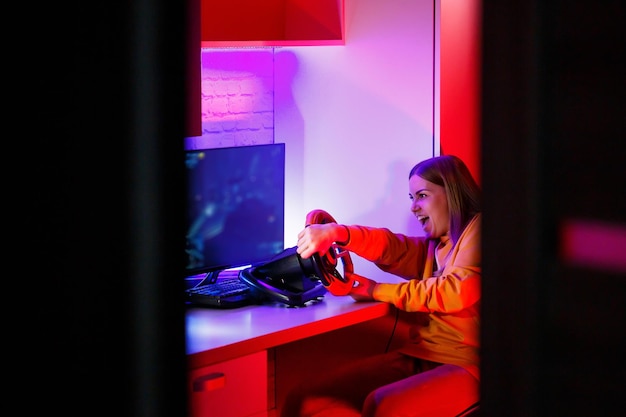 コンピューターでレースをしている女の子ゲーマー彼女はハンドルの感情的な遊びを使用しています