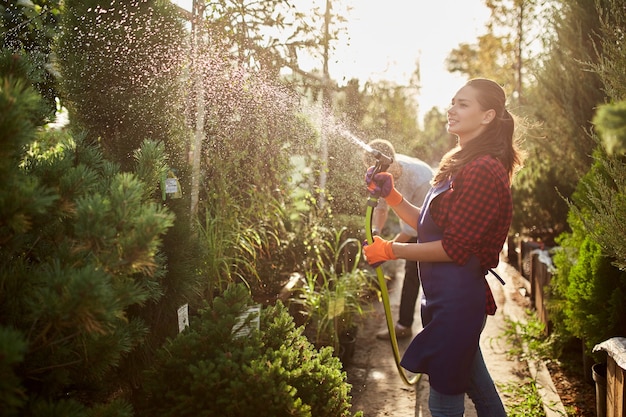 Girl gardener sprays water plants in the beautiful nursery-garden on a sunny day. Working in the garden .