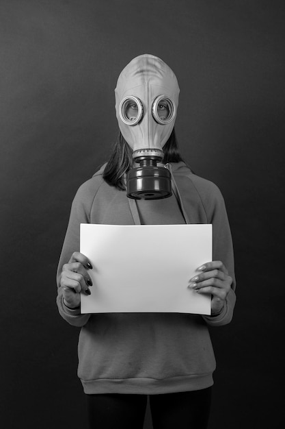 The girl in a gas mask on a black background holds a white sheet