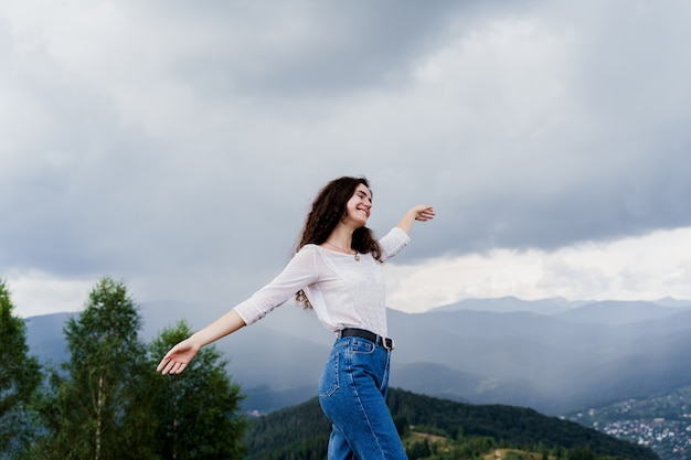 Girl girl raised her hands up and enjoys the mountain hills view.