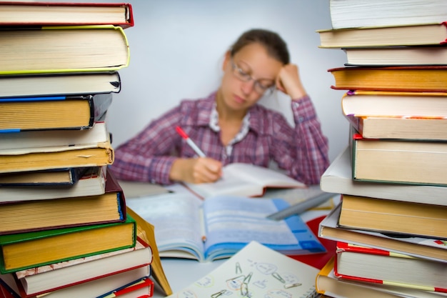 The girl in glasses is surrounded by books. Learning. Homework.