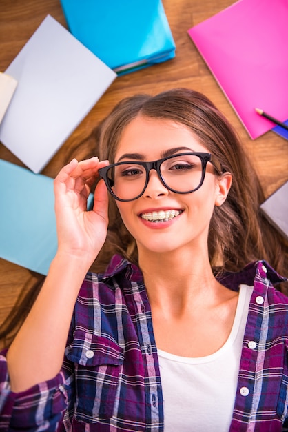 The girl in glasses lies on the floor and smiles.