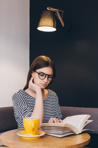 Girl in glasses reading a book in a coffee shop