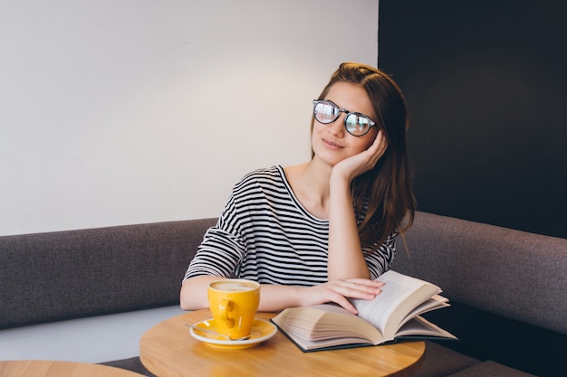 Girl in glasses reading a book in a coffee shop