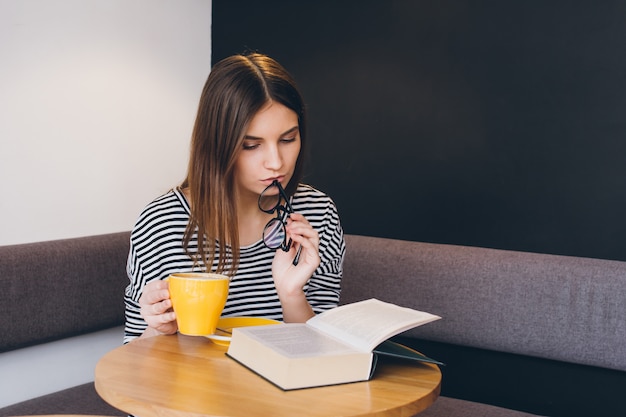 Girl in glasses reading a book in a coffee shop