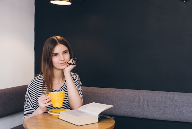 Girl in glasses reading a book in a coffee shop