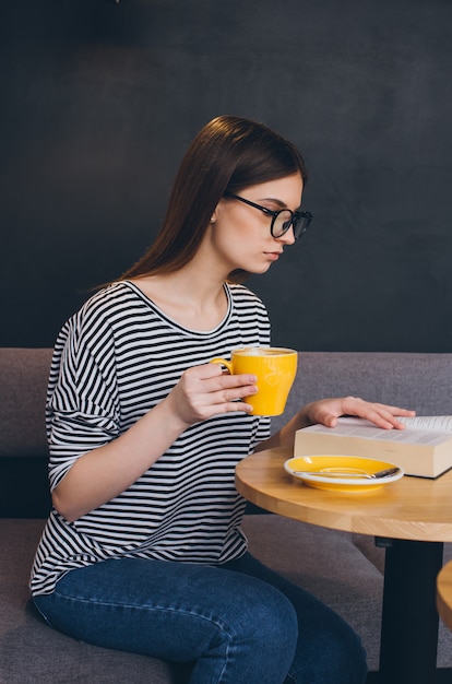 Девушка в очках читает книгу в кафе