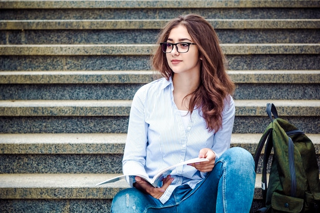 Foto una ragazza con gli occhiali con i libri è seduta sulle scale