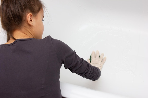 A girl in gloves washes a white bath with a foam sponge