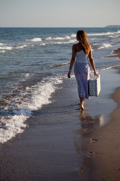 La ragazza va in spiaggia con una valigia in mano