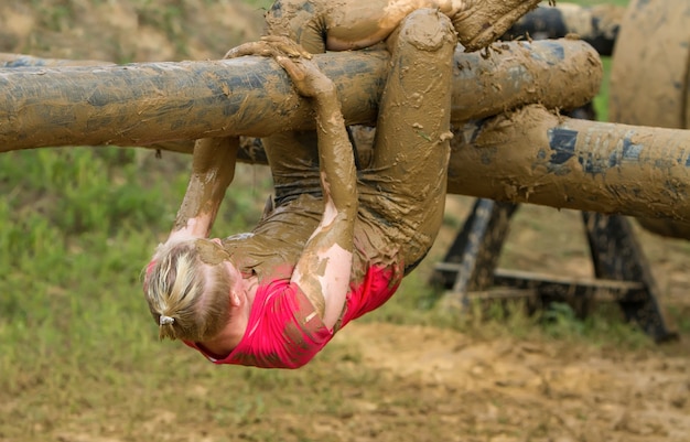 The girl goes through an obstacle on a slippery log from the mud.