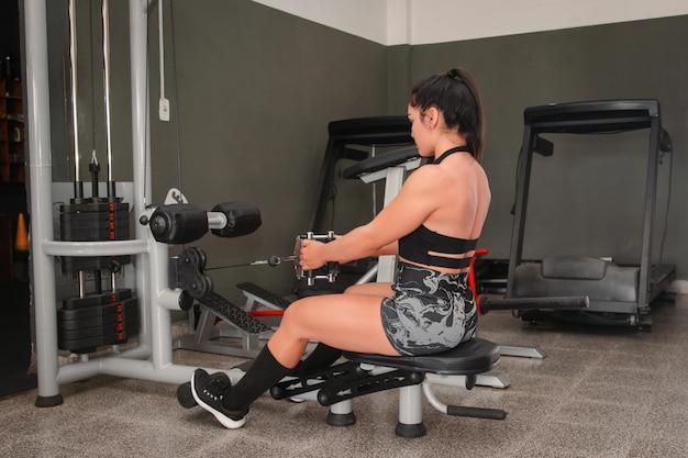 Photo girl in good physical condition performing back exercises with pulley in the gym