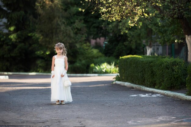 Ragazza laureata in un asilo in un abito bianco per strada