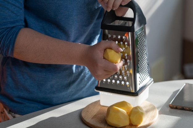 A girl grates freshly peeled potatoes for making potato pancakes