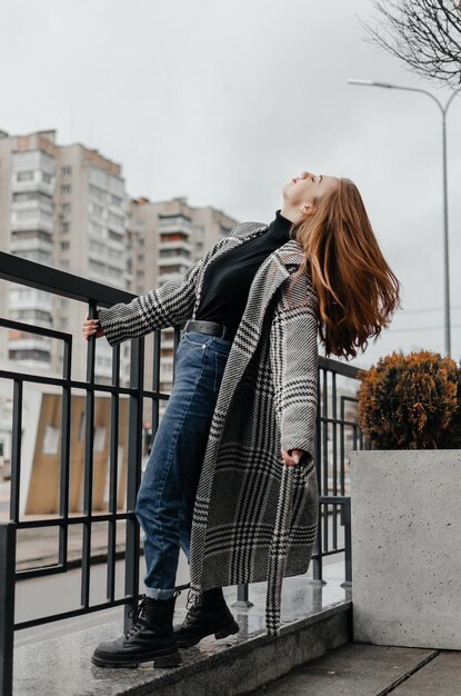 a girl in a gray coat and jeans holds on to the handrail