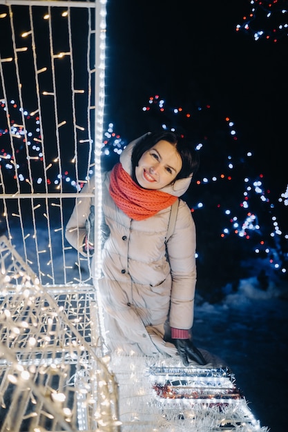 Девушка в серой куртке зимой с горящими вечерними огнями на Рождественской улице