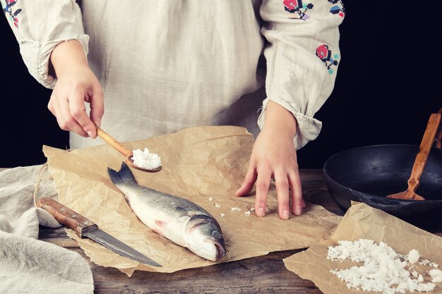 Girl in a gray long linen dress holds a full spoonful of salt