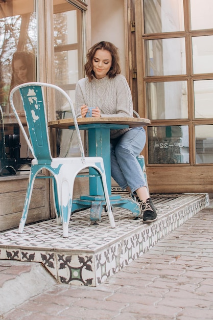 A girl in a gray sweater sits at a table in a coffee shop and drinks cocoa and enjoys the aroma