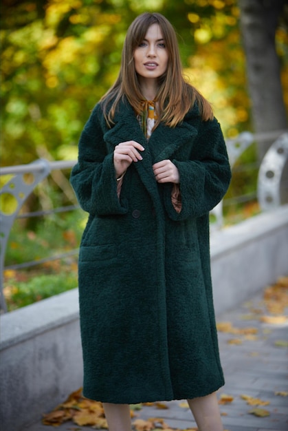 Foto ragazza con un cappotto verde sullo sfondo di un parco autunnale