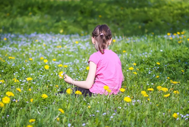 日光の下で野花がたくさんある緑の春の牧草地の女の子。自然を探検する子供。