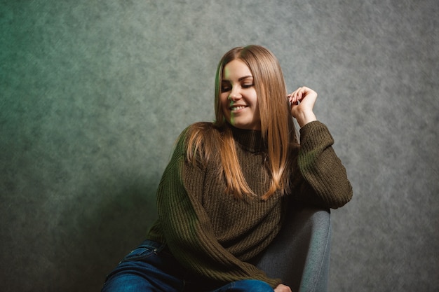 Girl in a green sweater and jeans on a gray chair and smiling