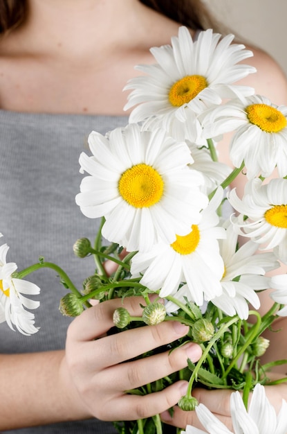 The girl in a grey dress holds a bouquet of white daisies in hand