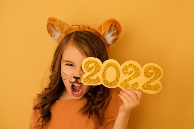 Girl in the guise of a tiger growls with her mouth open holding the number 2022 year in hands