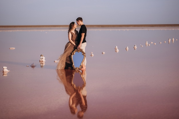 Girl and a guy on the shore of a pink salt lake at sunset