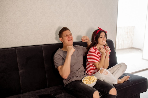 Girl and guy watching tv at home and eating popcorn