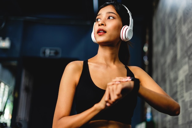 Ragazza in palestra esercizio ascoltare musica con cuffie overear bianche e utilizzare un esercizio sistematico timer battito cardiaco digitale gli esercizi sono strutturati