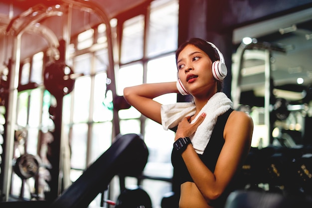 Ragazza in palestra esercizio utilizzando un telefono cellulare ascoltando musica con cuffie overear bianche e utilizzando un timer digitale del battito cardiaco esercizio sistematico il suo relax in vacanza